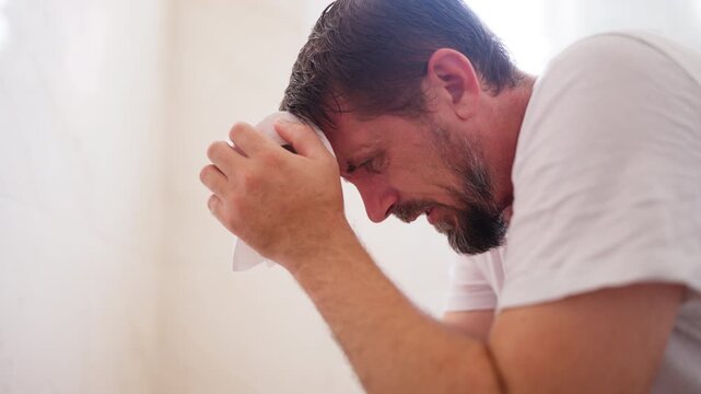 Sad bearded man sitting in a toilet and suffering from constipation or diarrhea, holding his stomach and a toilet paper roll while experiencing pain, discomfort, and cramps