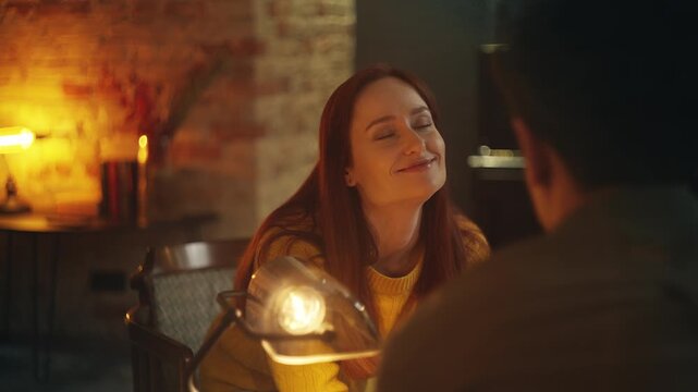 Smiling young woman listens to boyfriend's compliments, enjoying date in cafe