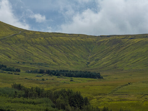 Aerial view of Keeloges featuring rolling green hills, patches of forest, and grassy slopes under a cloudy sky in County Donegal, Ireland.