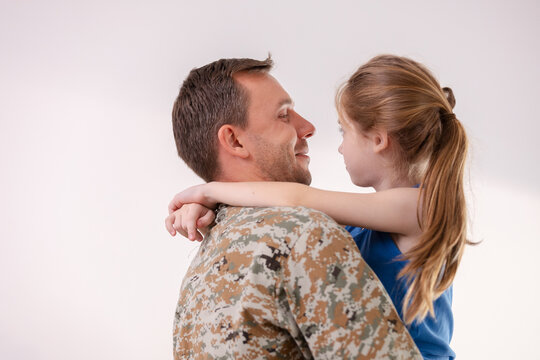 Happy soldier father sharing affectionate hug with cute young daughter during military return expressing deep love and joyful family reunion against plain white background