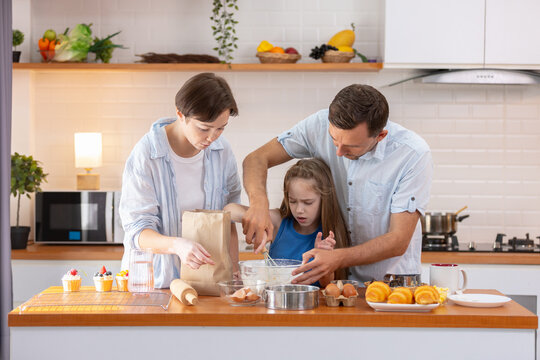 Happy family bonding in modern kitchen. Loving mother and supportive father help young child with baking sweet treats. Focused daughter enjoying cooking process while mixing flour in big bowl