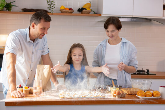 Happy family enjoying playful baking session in kitchen throwing flour. Joyful daughter with mother and father creating fun messy cloud while cooking homemade food together on weekend