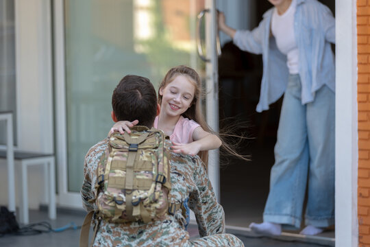 Happy military soldier father returns home sharing joy filled reunion and warm hug with lovely smiling daughter while loving family watches from doorway