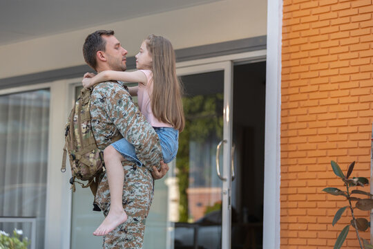 Loving soldier father holding young daughter during emotional reunion at home wearing military army uniform expressing deep joy and affection after long deployment away from family