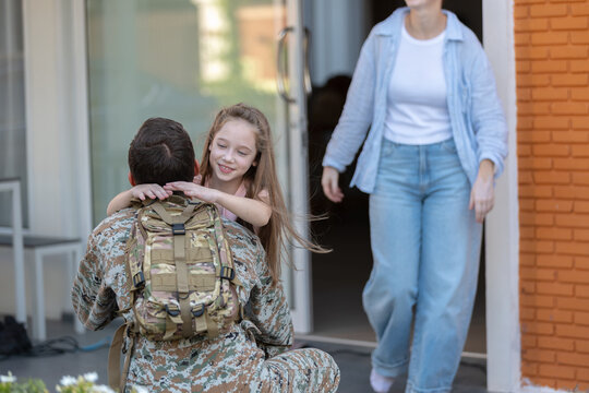 Happy soldier returning home hugging joyful daughter during emotional family reunion while mother watches military father arriving safely at brick house porch displaying deep love and affection