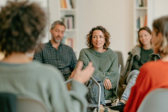 Woman with curly afro hair speaking in a support group circle, featuring chunky knit textures and a soft muted mood for therapy and community workshops