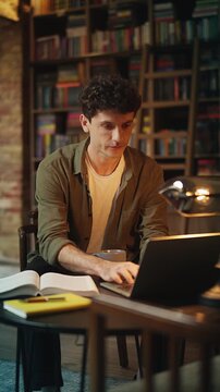 Male scientist conducts research in urban library, using laptop and reading book