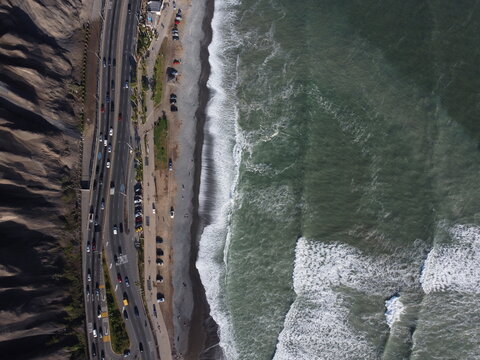 Aerial view of the Costa Verde coastline with a busy highway running alongside the beach, crashing waves, and steep cliffs in Miraflores, Provincia de Lima, Peru.