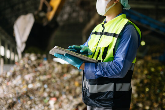 Environmental engineer in protective safety gear inspecting processed waste and taking notes on a clipboard at an industrial recycling facility.