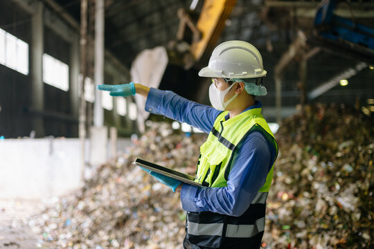 Environmental engineer in protective safety gear inspecting processed waste and taking notes on a clipboard at an industrial recycling facility.