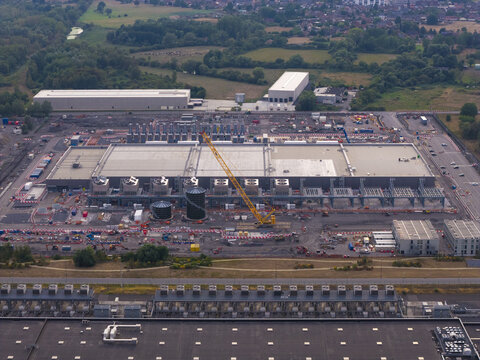 Aerial view of a hyperscale data center under construction with a yellow crane, cooling units, and industrial infrastructure in Belgium.