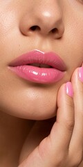 Naklejka premium A close-up photo of a girl's glossy pink lips, her hand on her cheek, and pink glossy nail polish against a studio backdrop.