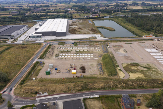 Aerial view of the construction site for a Battery Energy Storage System featuring concrete foundations and equipment containers in a rural industrial area in Belgium.