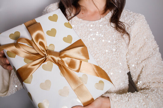 Woman brunette with shiny gift box wrapped in festive paper with big golden bow close up. Celebration mood, making presents. Christmas party vibe.