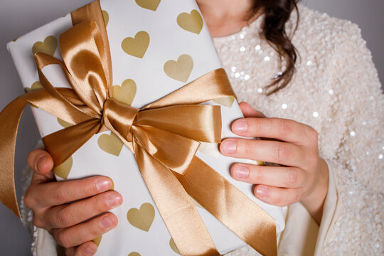 Woman with shiny gift box wrapped in festive paper with big golden bow. Celebration mood, making presents. Christmas party vibe.