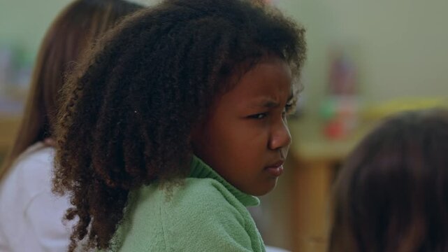 African child in classroom with curly hair green sweater thoughtful girl among classmate during school learning activity education desk quiet expression