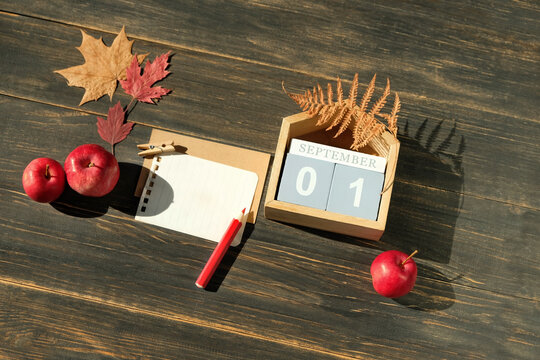 September calendar. calendar block with date 1 September, pencils, empty note paper, dry fallen leaves and red apples close up on brown wooden table background. copy space. Template for design