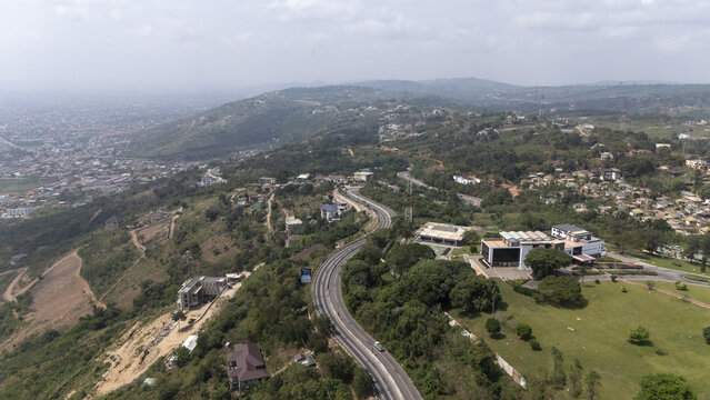 Aerial view of the winding road through the lush green hills of the Aburi mountains with scattered buildings and distant urban sprawl in Aburi, Eastern Region, Ghana.