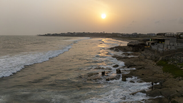 Aerial view of Sakumono Beach at sunset with waves crashing against the rocky shoreline and golden light reflecting on the water in Sakumono, Greater Accra Region, Ghana.