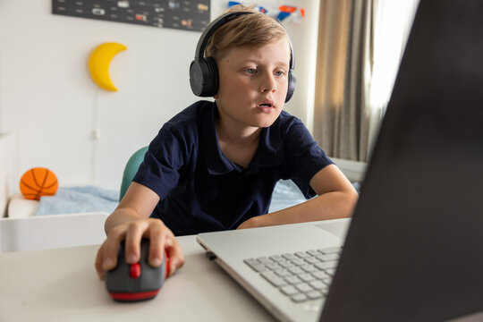 Boy with headphones using laptop at home in his room. Gaming, learning, music listening or browsing internet
