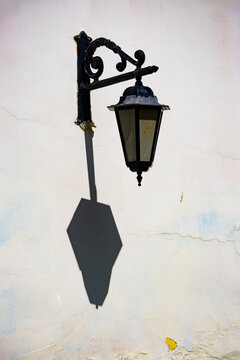 Ornate wall lantern casting long shadow on weathered plaster wall