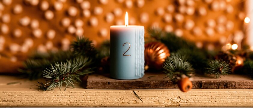 Blue advent candle with numeral two on a rustic wooden plank, surrounded by fir branches and ornaments for holiday banners and winter decor