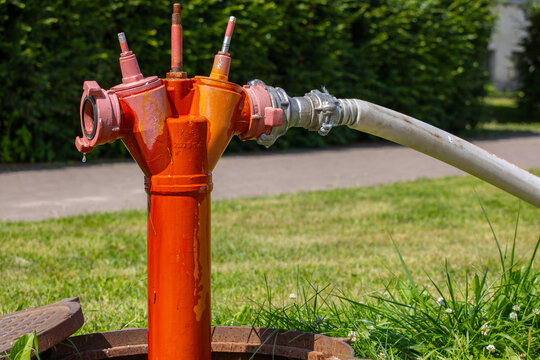 Orange fire hydrant connected to a hose for water supply outdoors