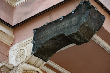 Protective netting draped over an ornate cornice on historic facade © Mariia