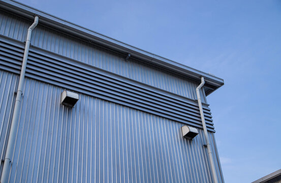 Industrial building facade with metal sheet wall, rain gutter downspouts, and ventilation hood exhausts