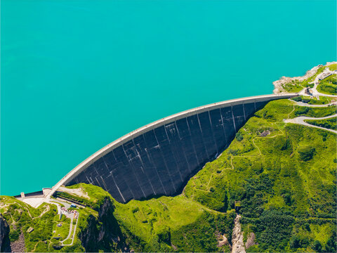 Aerial view of Stausee Mooserboden dam with its curved concrete wall holding back vibrant turquoise reservoir water, surrounded by lush green alpine slopes Kaprun, Salzburg, Austria.