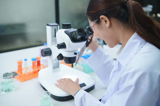 Scientist Conducting Chemical Experiment Using Microscope and Pipette in Laboratory