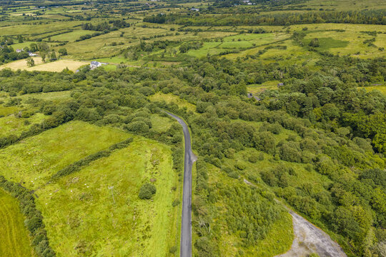 Aerial view of the rural landscape of Keeloges, featuring a narrow road winding through lush green fields, dense thickets of trees, and rolling hills in County Donegal, Ireland.