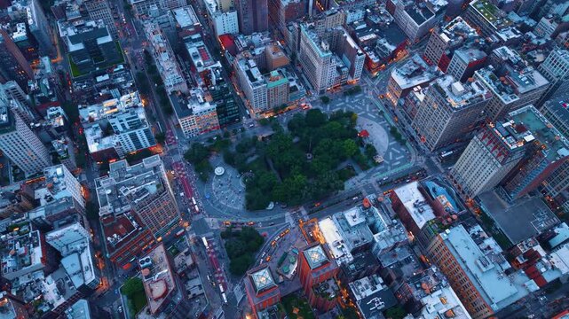 Overhead view of Union Square park and buildings, New York. Straight down aerial framing green trees, surrounding road intersections and lighted urban blocks at dusk.