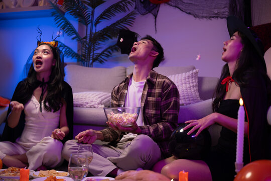 Young Asian friends eating popcorn and snacks during a Halloween party.