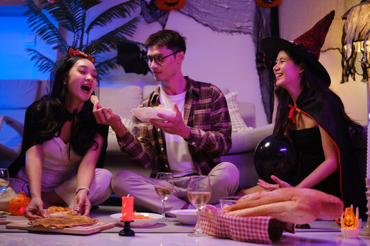 Young Asian friends eating popcorn and snacks during a Halloween party.