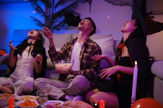 Young Asian friends eating popcorn and snacks during a Halloween party.