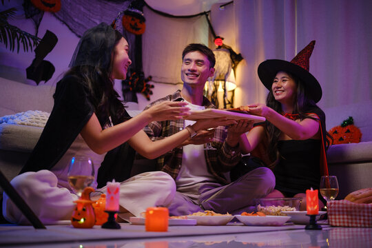 Young Asian friends sharing pizza together at a Halloween costume party.
