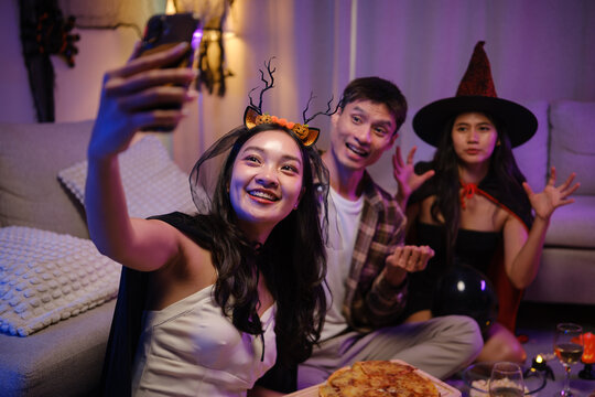 Young Asian friends taking a smartphone selfie with pizza at a Halloween party.