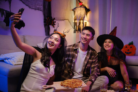 Young Asian friends taking a smartphone selfie with pizza at a Halloween party.