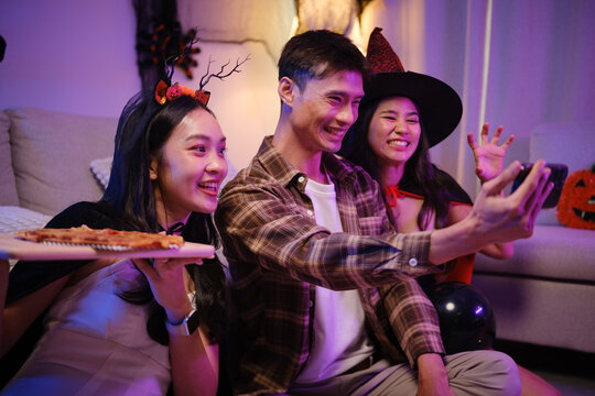 Young Asian friends taking a smartphone selfie with pizza at a Halloween party.