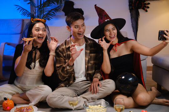 Young Asian friends taking a smartphone selfie with pizza at a Halloween party.