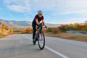 Naklejka premium Female Cyclist Training On Road Bike Through Mountain Landscape At Speed For Fitness And Endurance