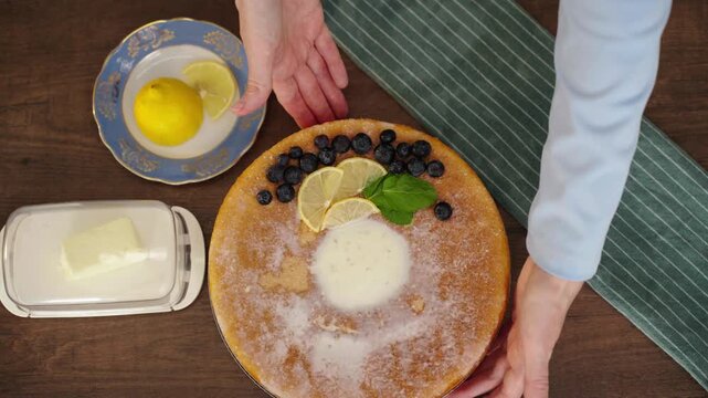 Hand presenting finished lemon blueberry cake in cozy kitchen