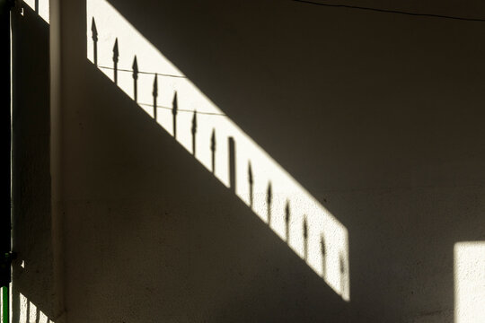 Shadows of a wrought iron fence cast on a textured wall during golden hour
