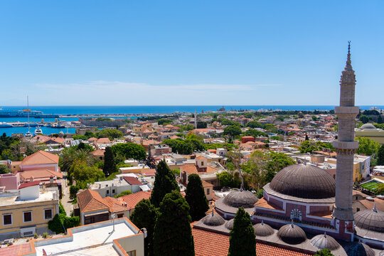 Rhodes, Greece - 16 May 2026: View of Suleymaniye Mosque with its distinctive minaret and dome, surrounded by historic terracotta rooftops, lush cypress trees, and the blue Aegean Sea.