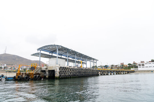 Chancay, Lima Region, Peru - 28 August 2024: View of Puerto Chancay featuring a modern metal pier structure with tire fenders along the waterfront under an overcast sky.