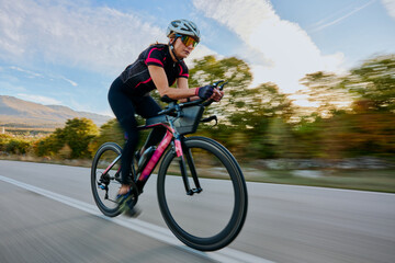 Naklejka premium Female Cyclist Racing on Road Bike at Speed Through Countryside During Sunset Training Ride