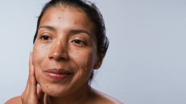 Closeup shot of young Hispanic woman applying cosmetic serum with dropper on face and massaging skin. Clip is ideal for skincare product marketing and beauty e-commerce campaigns