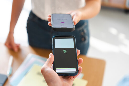 A customer makes a contactless payment by tapping their smartphone against the merchant's mobile device. This modern transaction happens in a retail shop setting.
