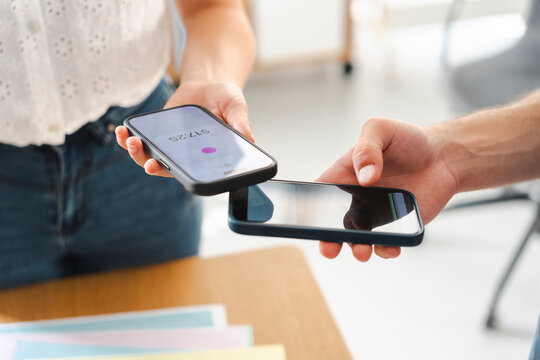 A customer uses a mobile phone to make a contactless payment at a small business counter. The merchant holds their device to process the transaction securely.
